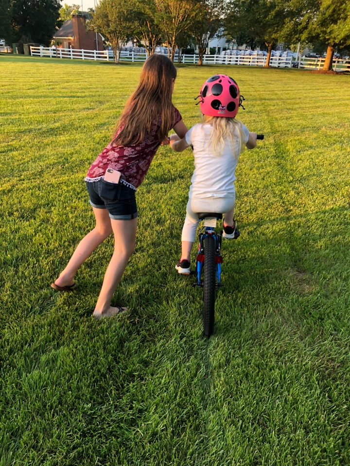 Big sister shows little sister how to ride a big girl bike.